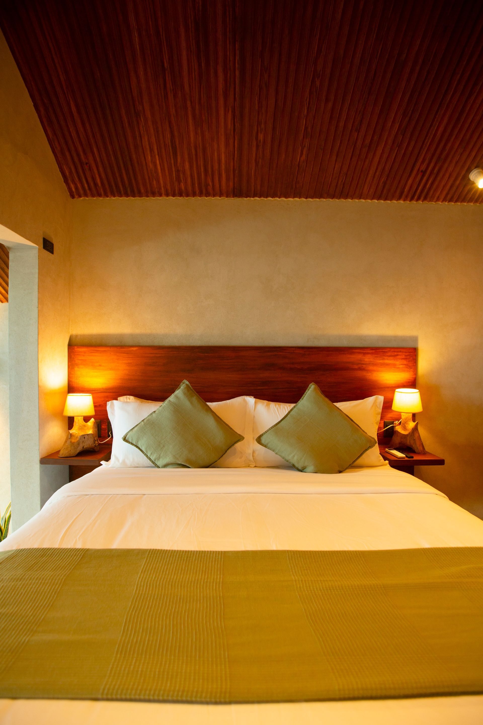 A hotel room with a king size bed and green pillows.