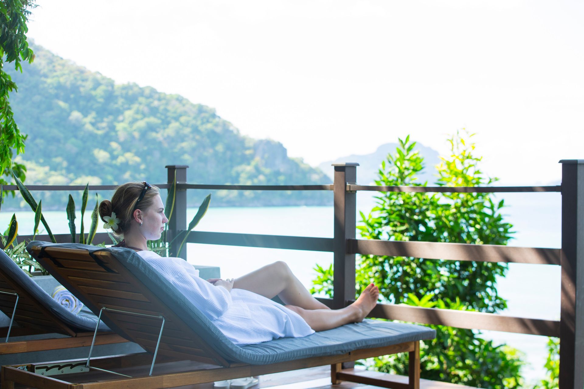 A woman is laying on a lounge chair on a balcony overlooking the ocean.
