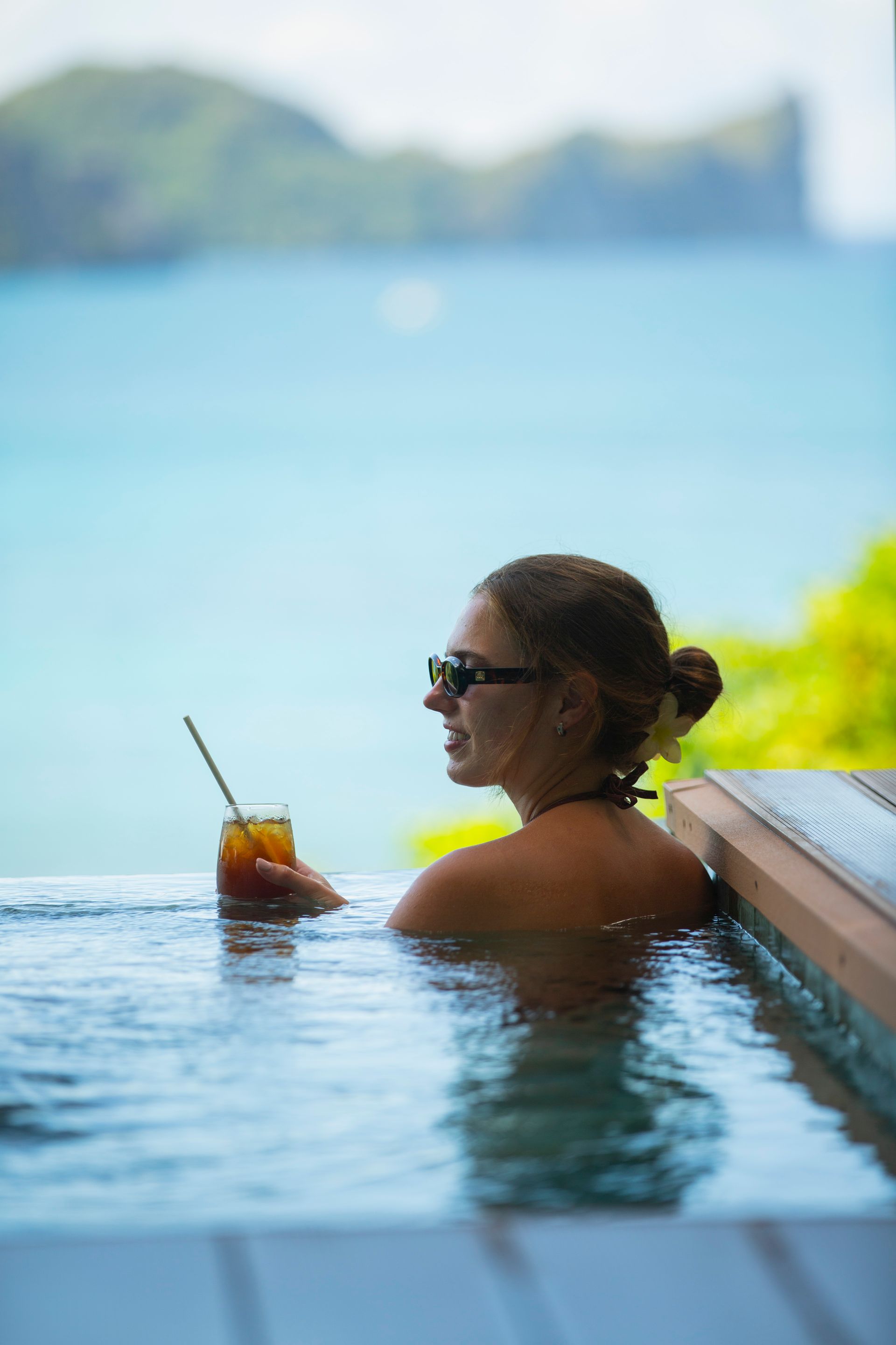 A woman is sitting in a swimming pool holding a drink.