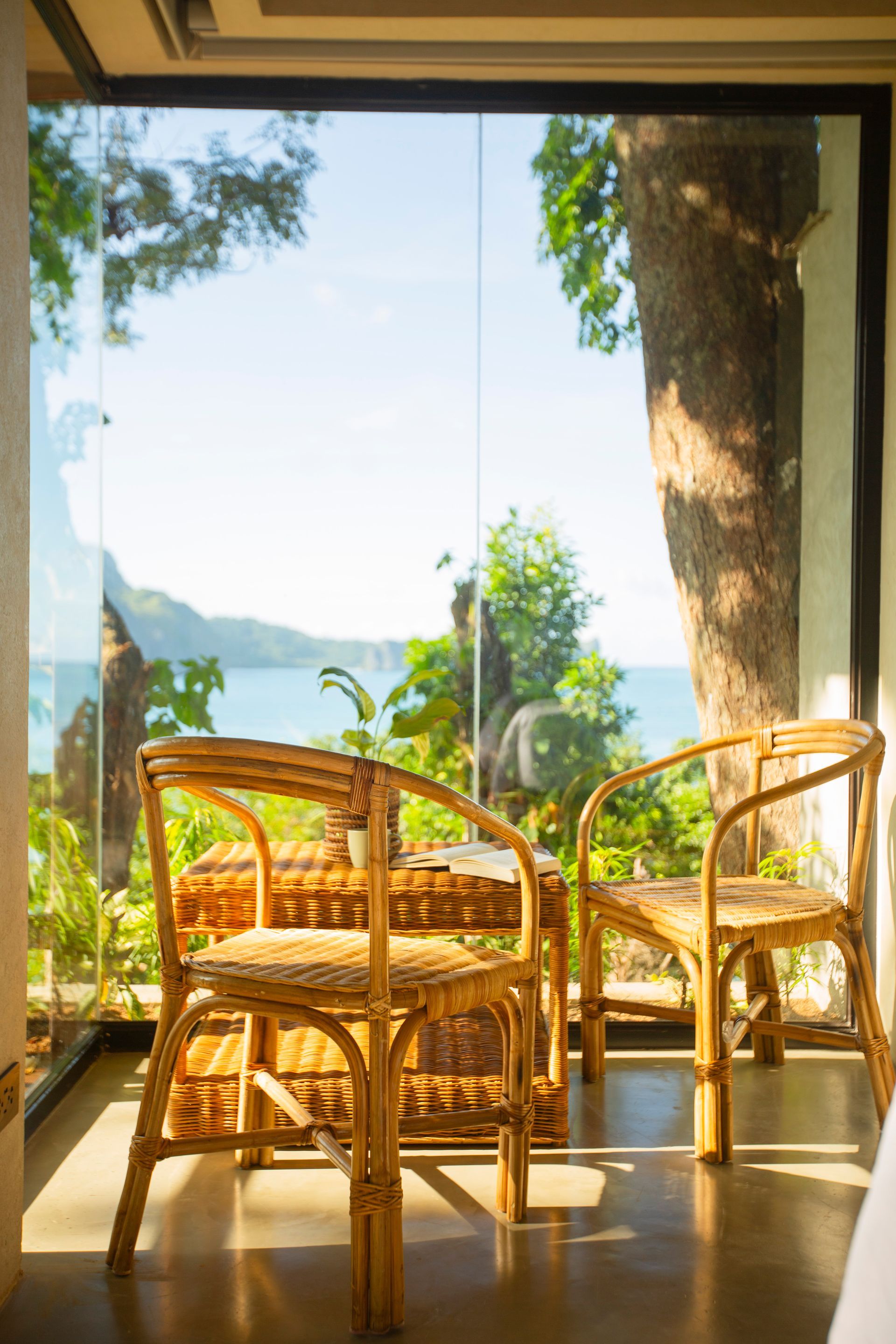 Two wicker chairs are sitting in front of a window with a view of the ocean.