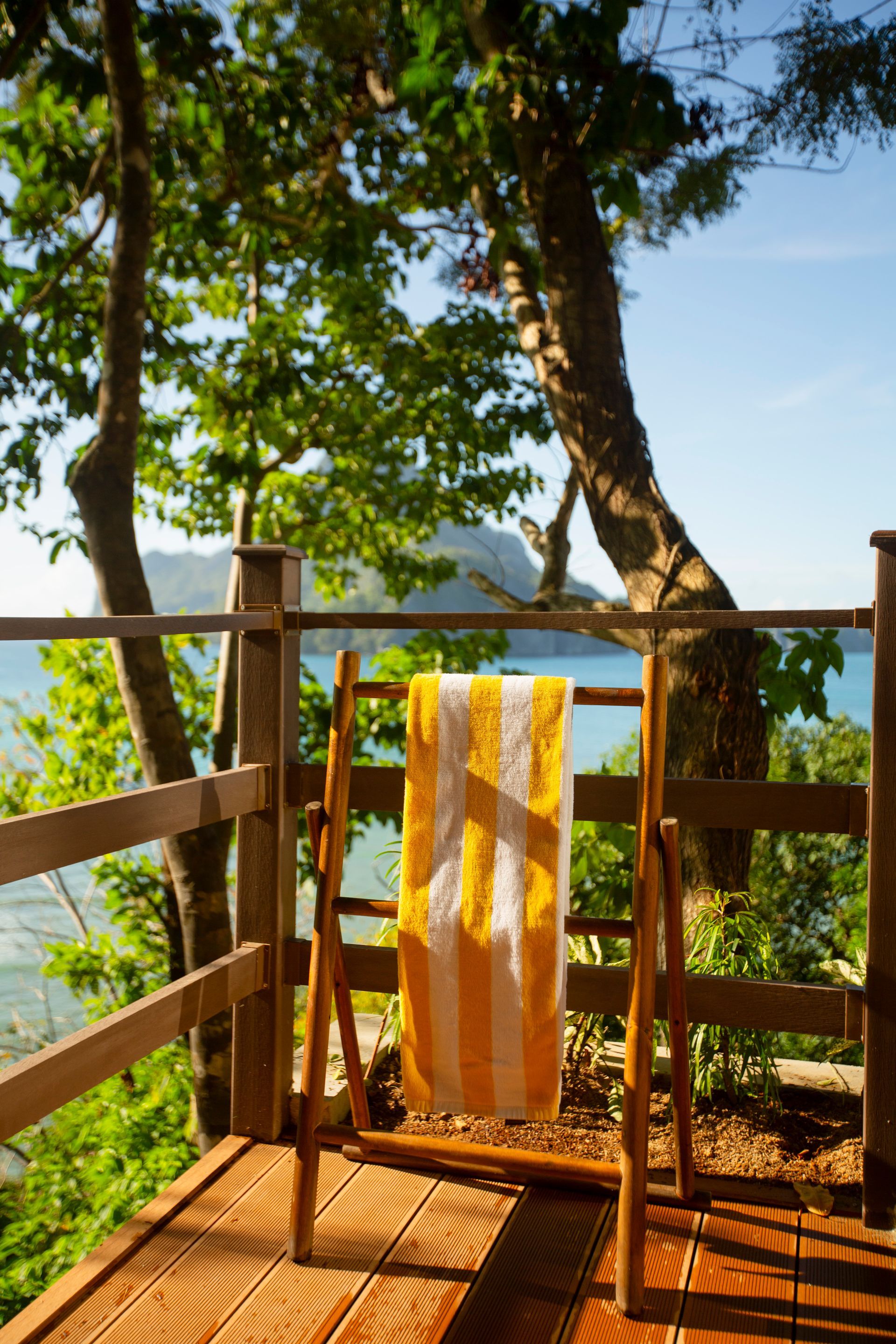 A yellow and white striped towel is hanging on a wooden railing overlooking the ocean.