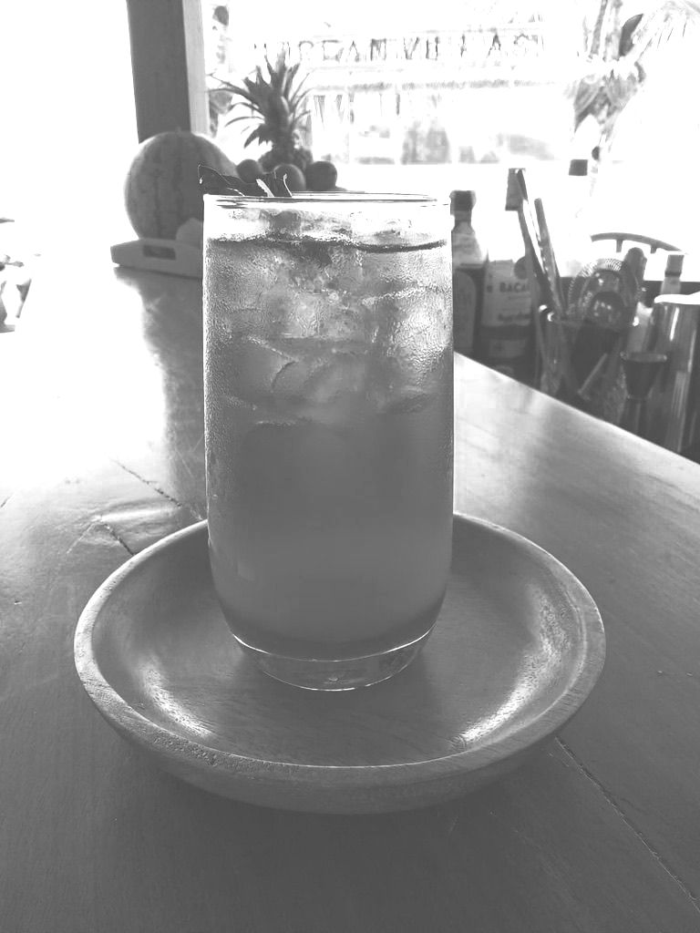 A black and white photo of a glass of iced tea on a saucer on a table.