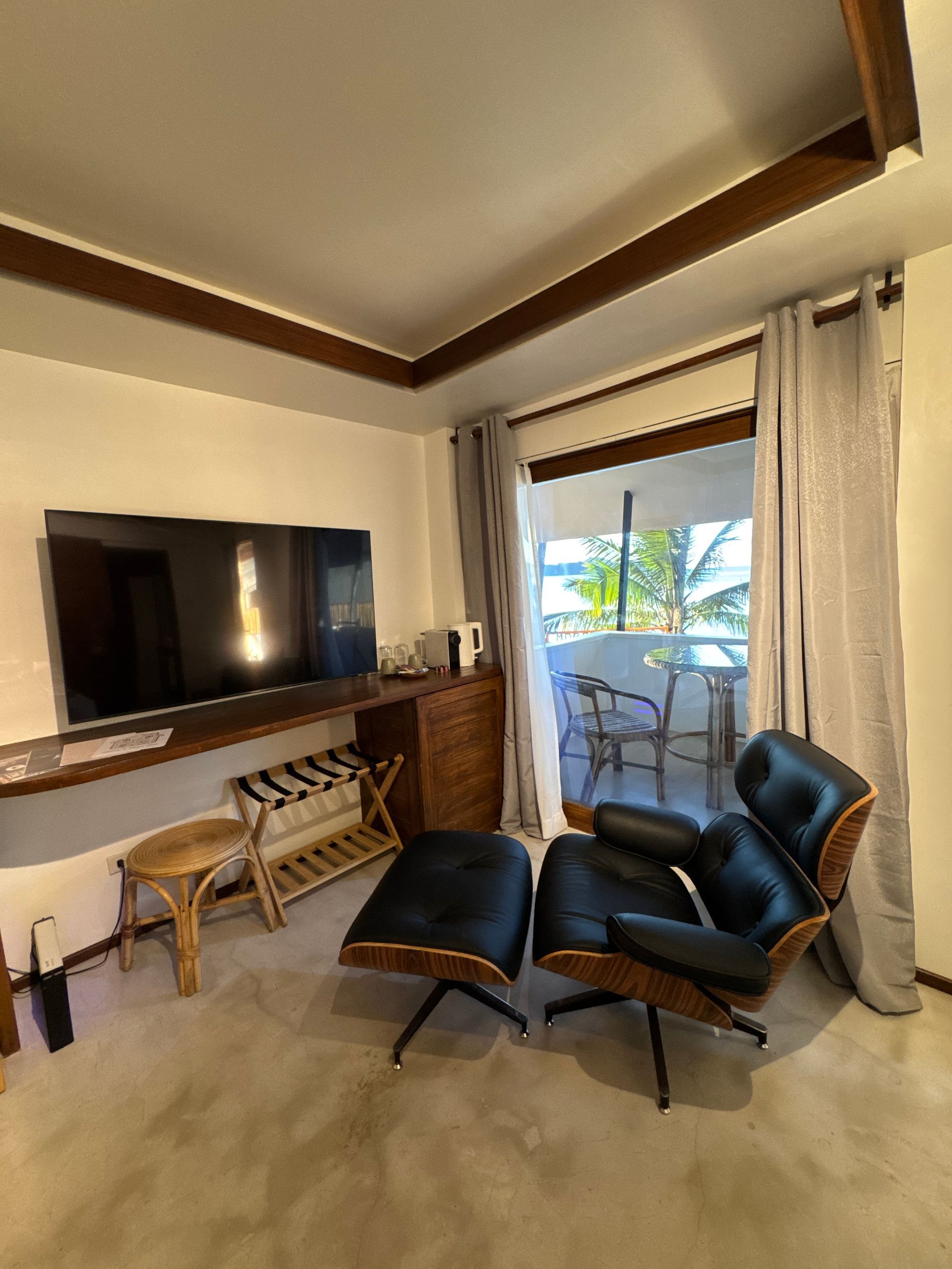 A living room with a chair , ottoman , television and a sliding glass door.
