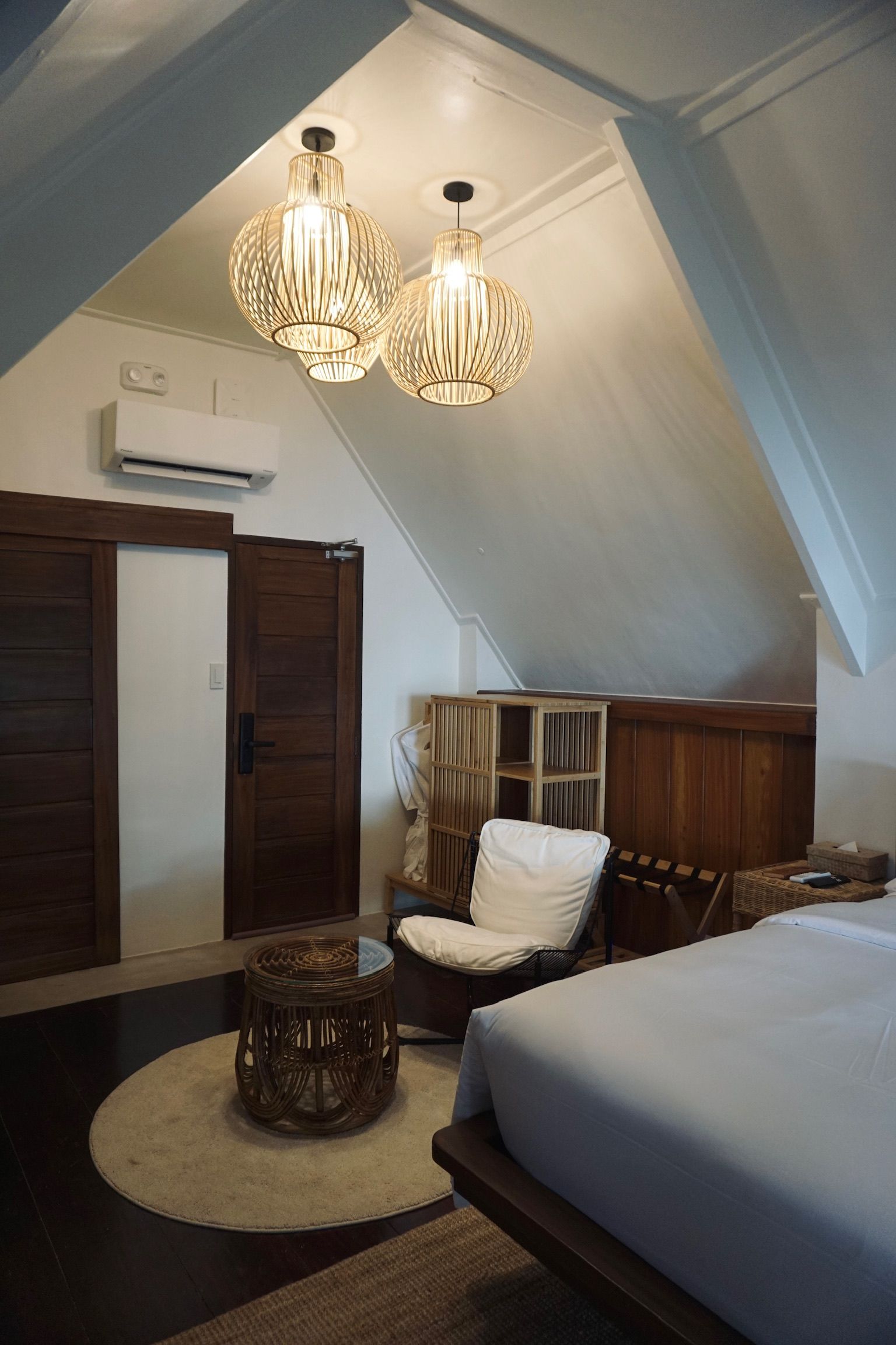 A bedroom with a bed , chair , table and two chandeliers hanging from the ceiling.