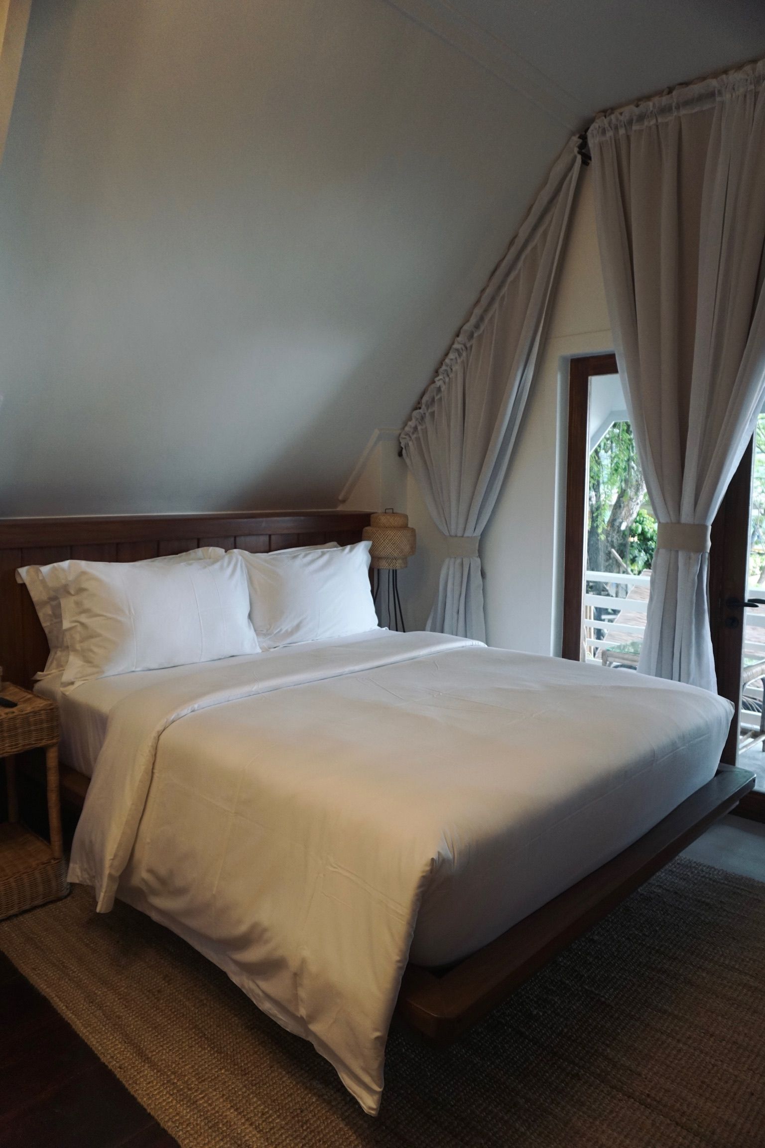 A bed with white sheets and pillows in a bedroom next to a window.