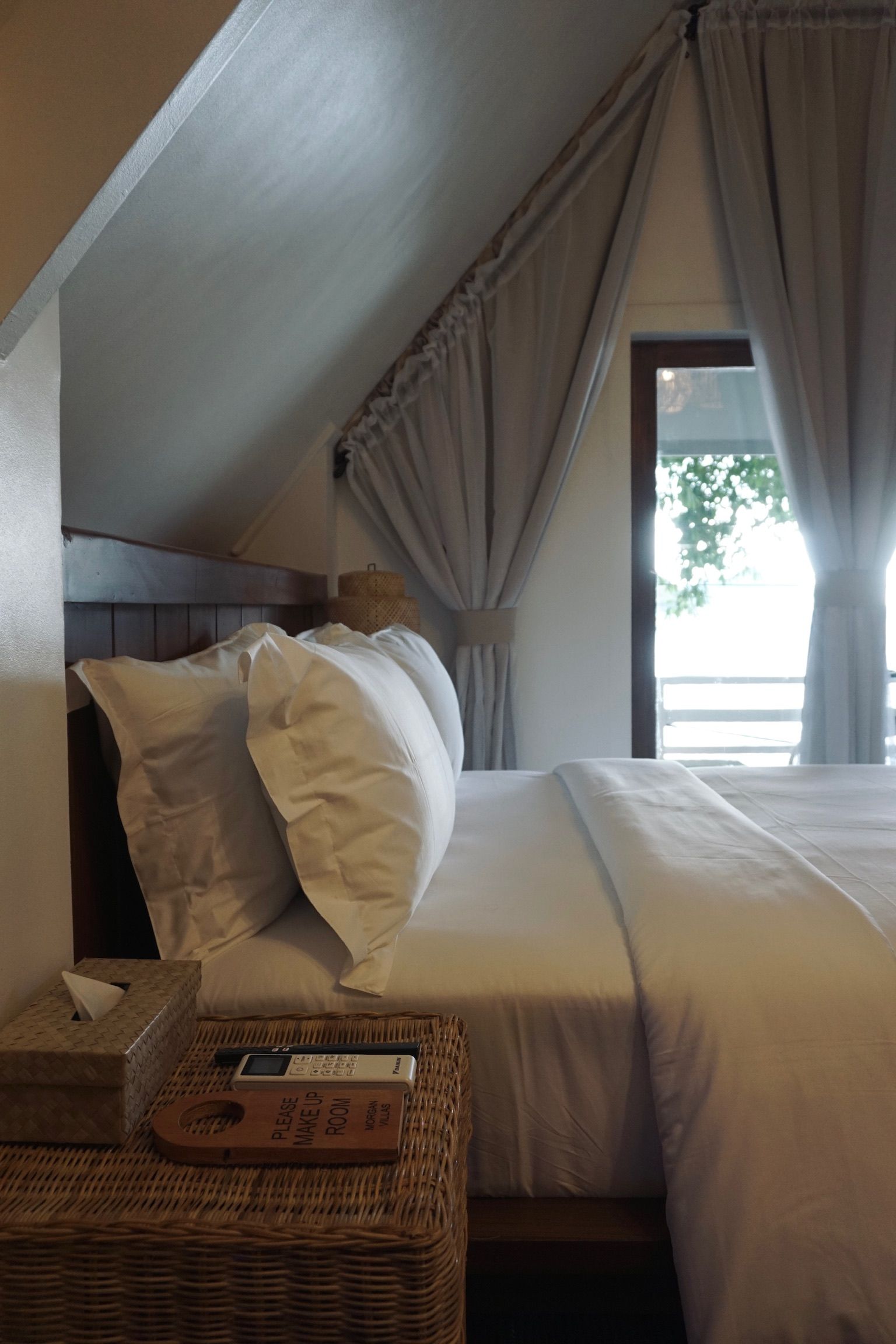 A bed with white sheets and pillows in a bedroom with a window.