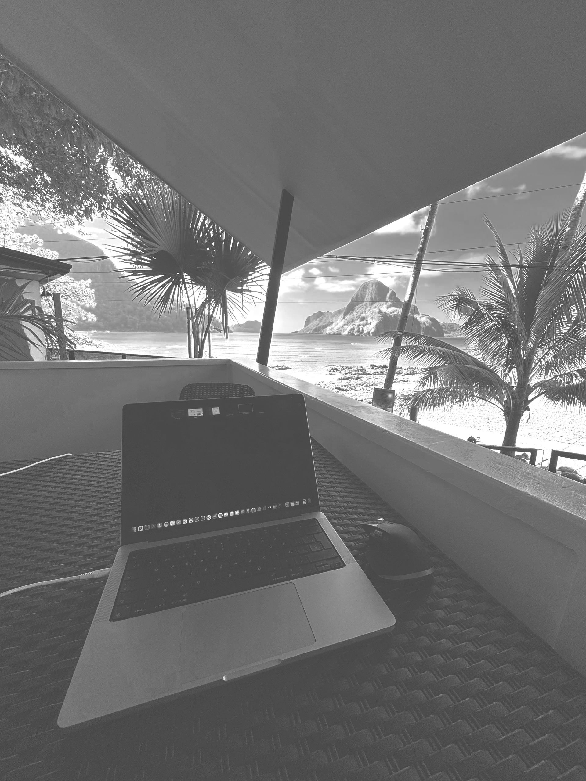 A black and white photo of a laptop on a balcony overlooking the ocean