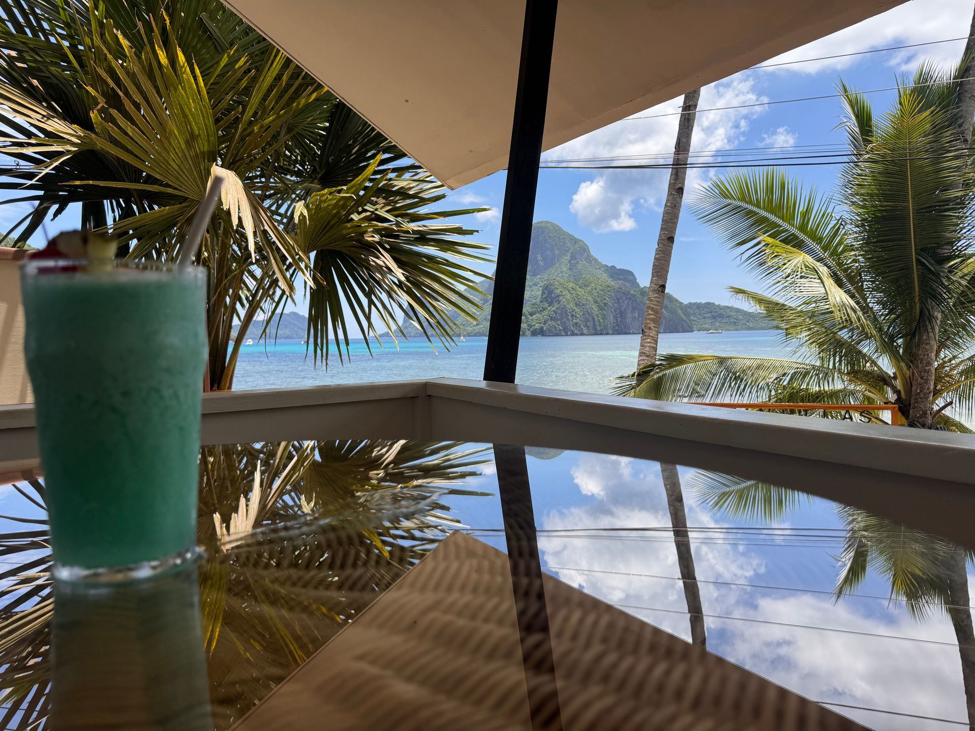 Room 2 . A blue drink sits on a table with palm trees in the background