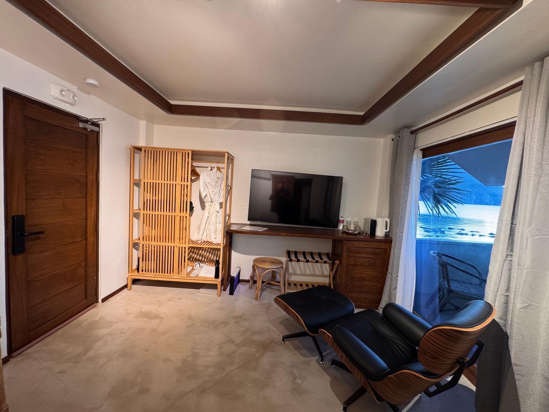 A living room with a chair , desk , television and a large window.