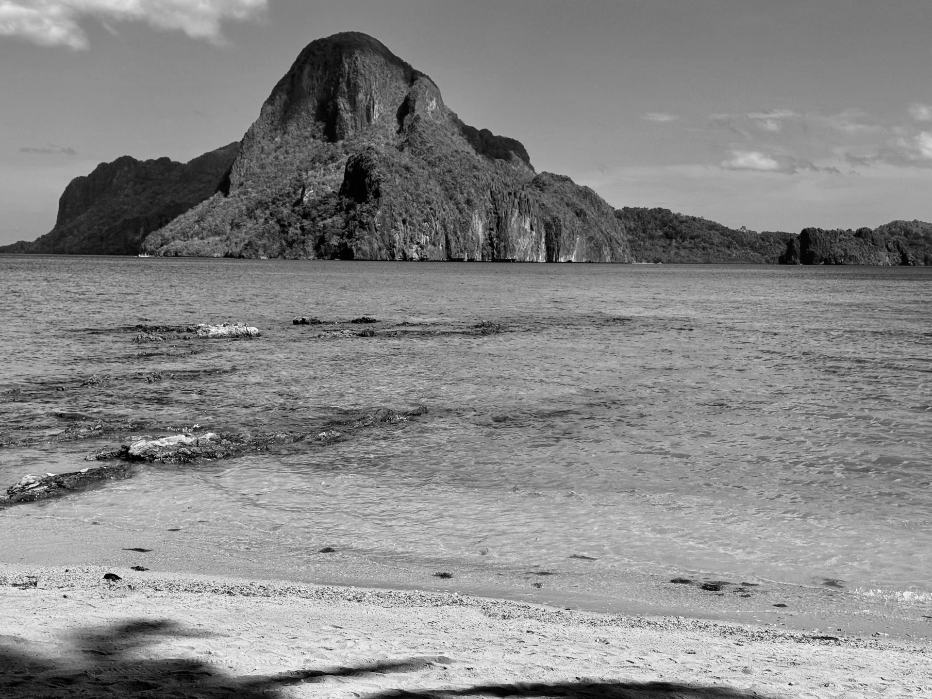 A black and white photo of a beach with a mountain in the background