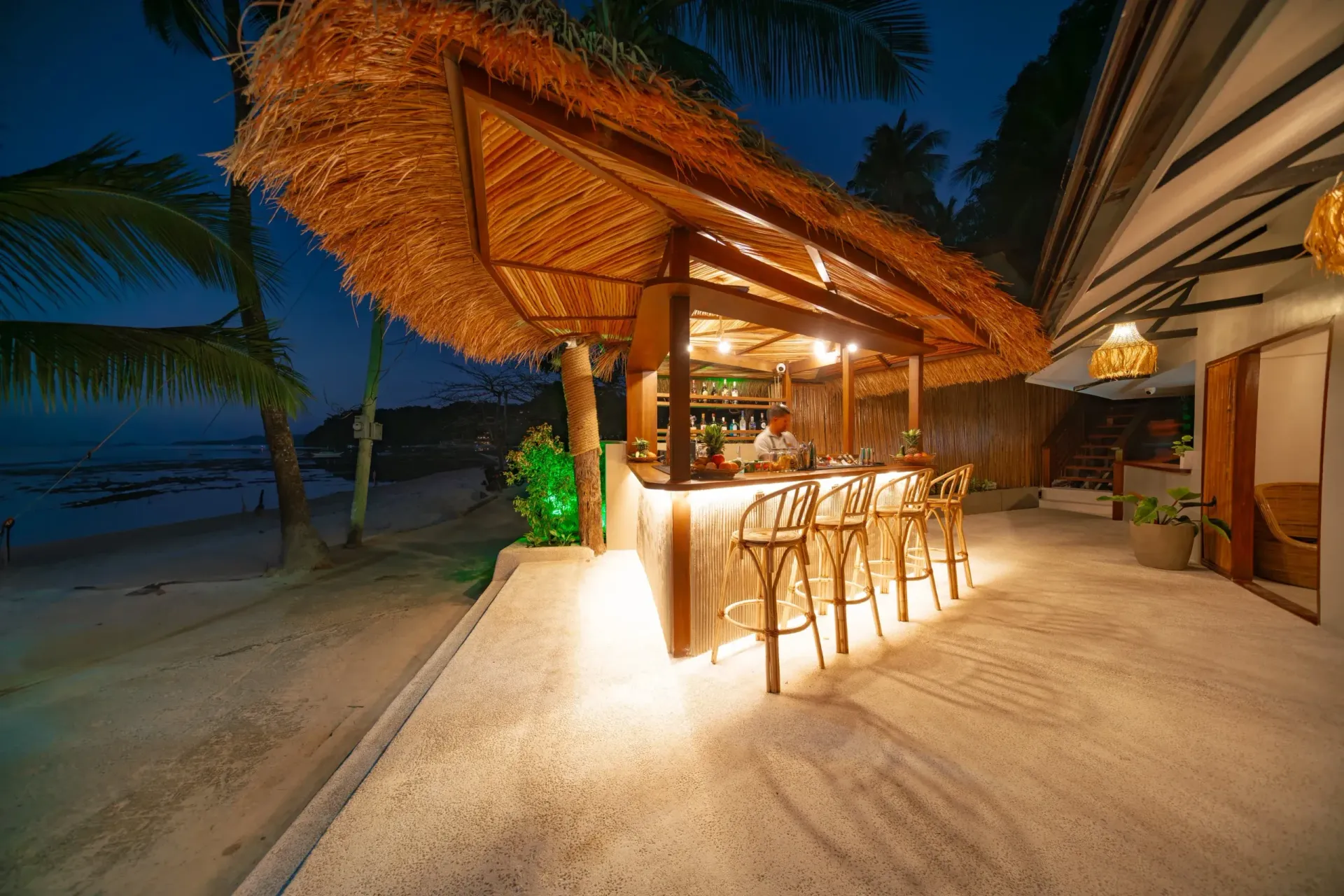 A beach bar with a thatched roof is lit up at night.