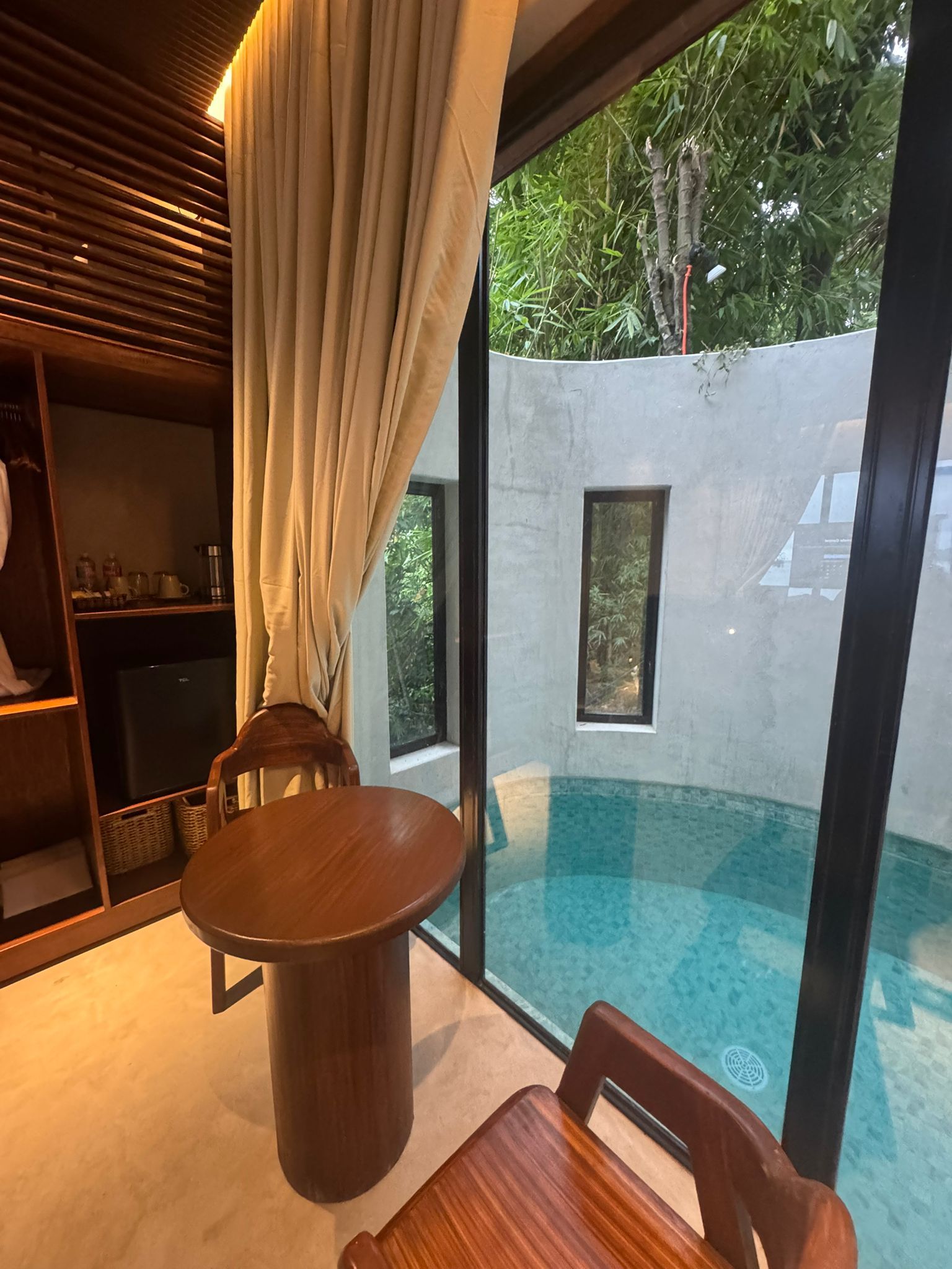 Interior with pool view, table and chairs. Wooden tones, light curtains, and a pool.