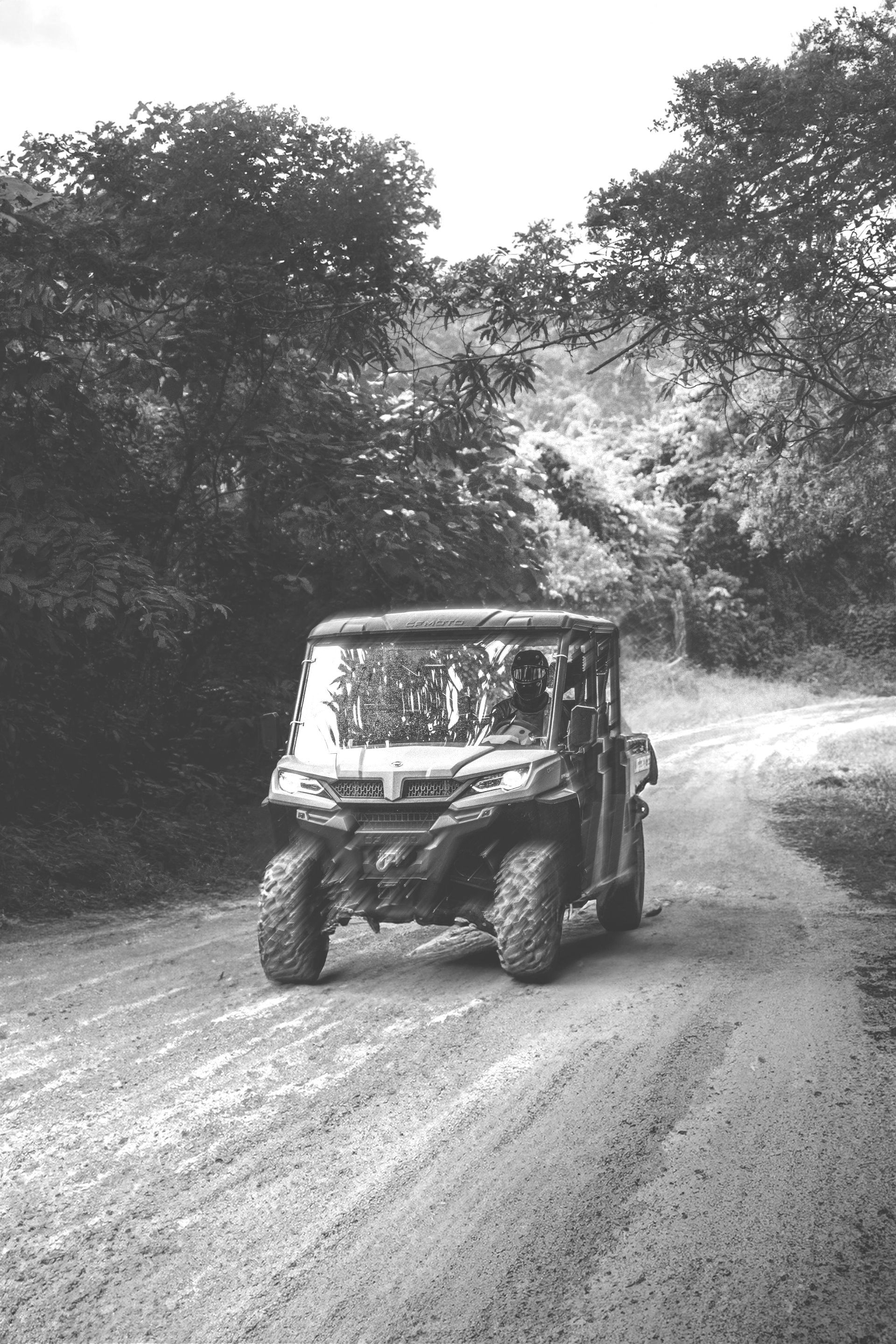 A black and white photo of a atv driving down a dirt road.