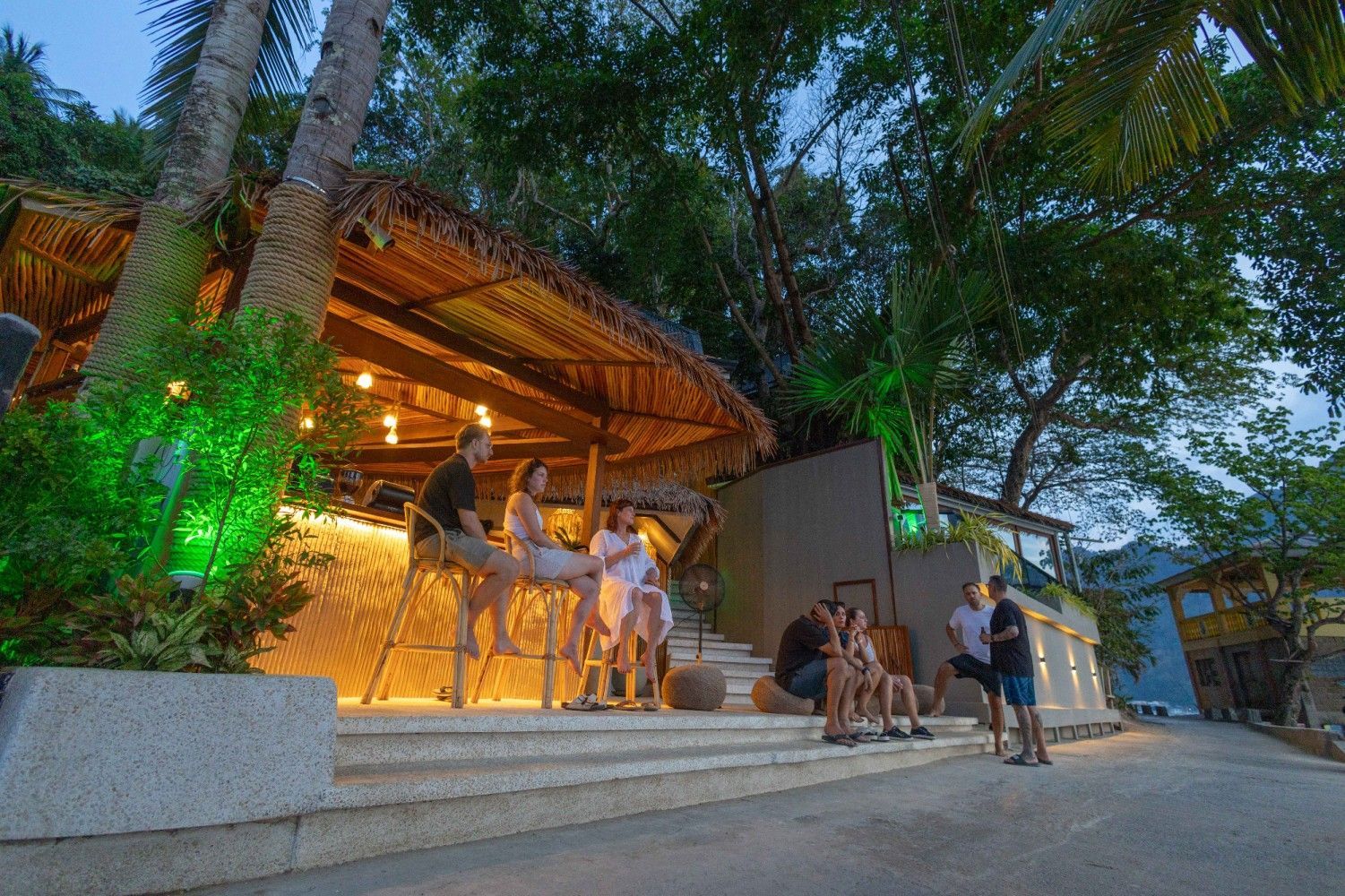 A group of people are sitting at a bar under a thatched roof.