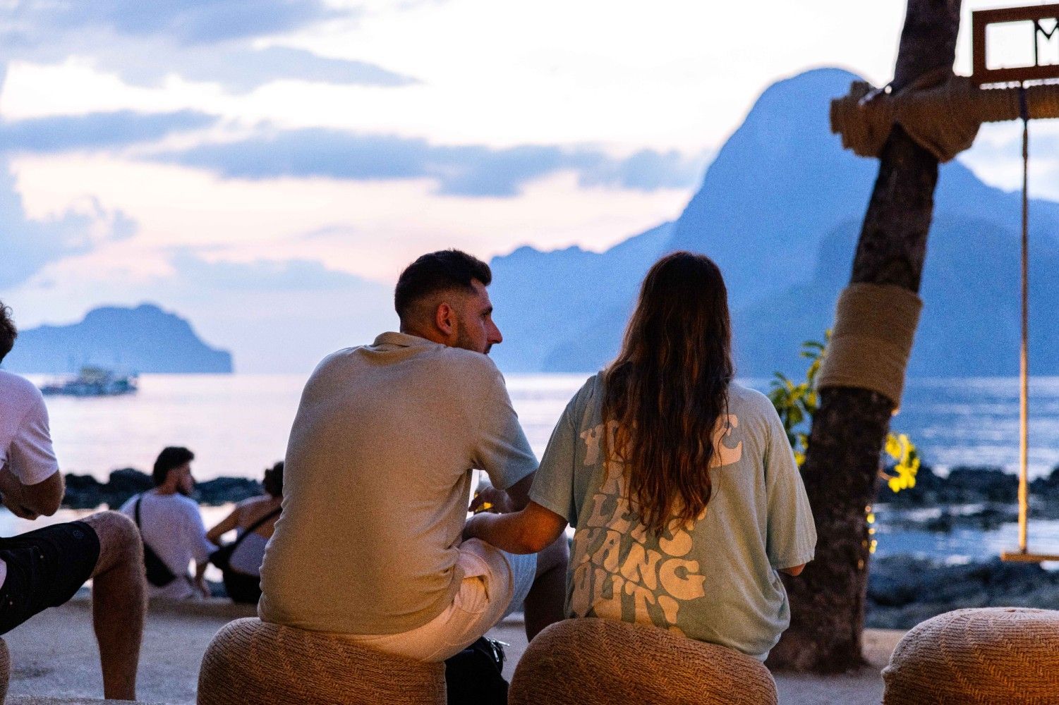 A man and a woman are sitting on rocks on the beach looking at the ocean.