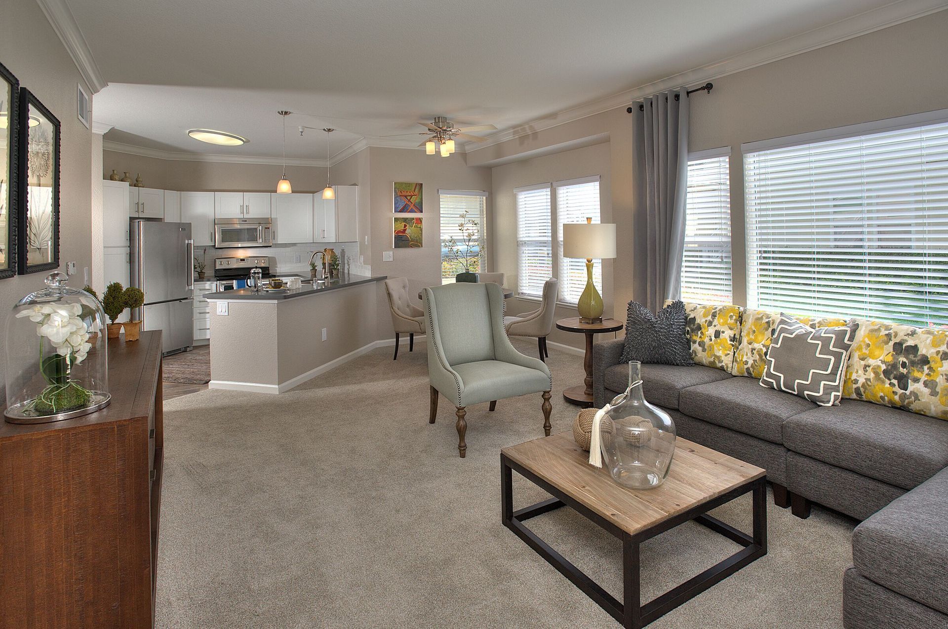 Cozy living room with open kitchen, gray sectional, wooden coffee table, and large windows.