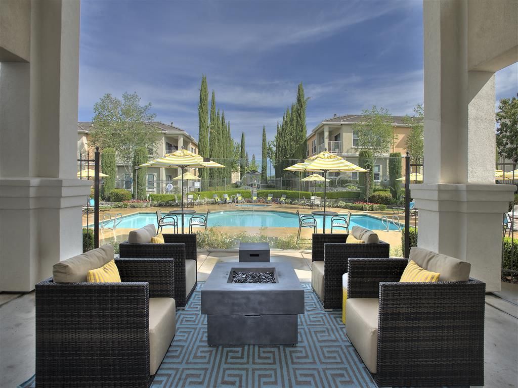 Outdoor community pool area with lounge seating under a covered patio and yellow umbrellas.