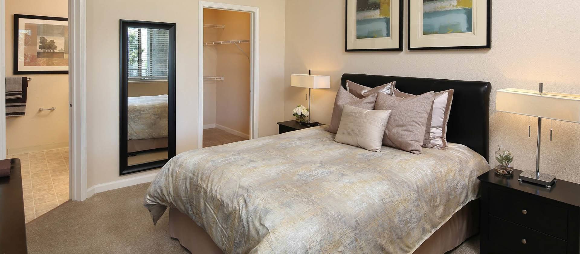 A bedroom with a bed, nightstands, a mirror, and an open closet. The walls are neutral colored.