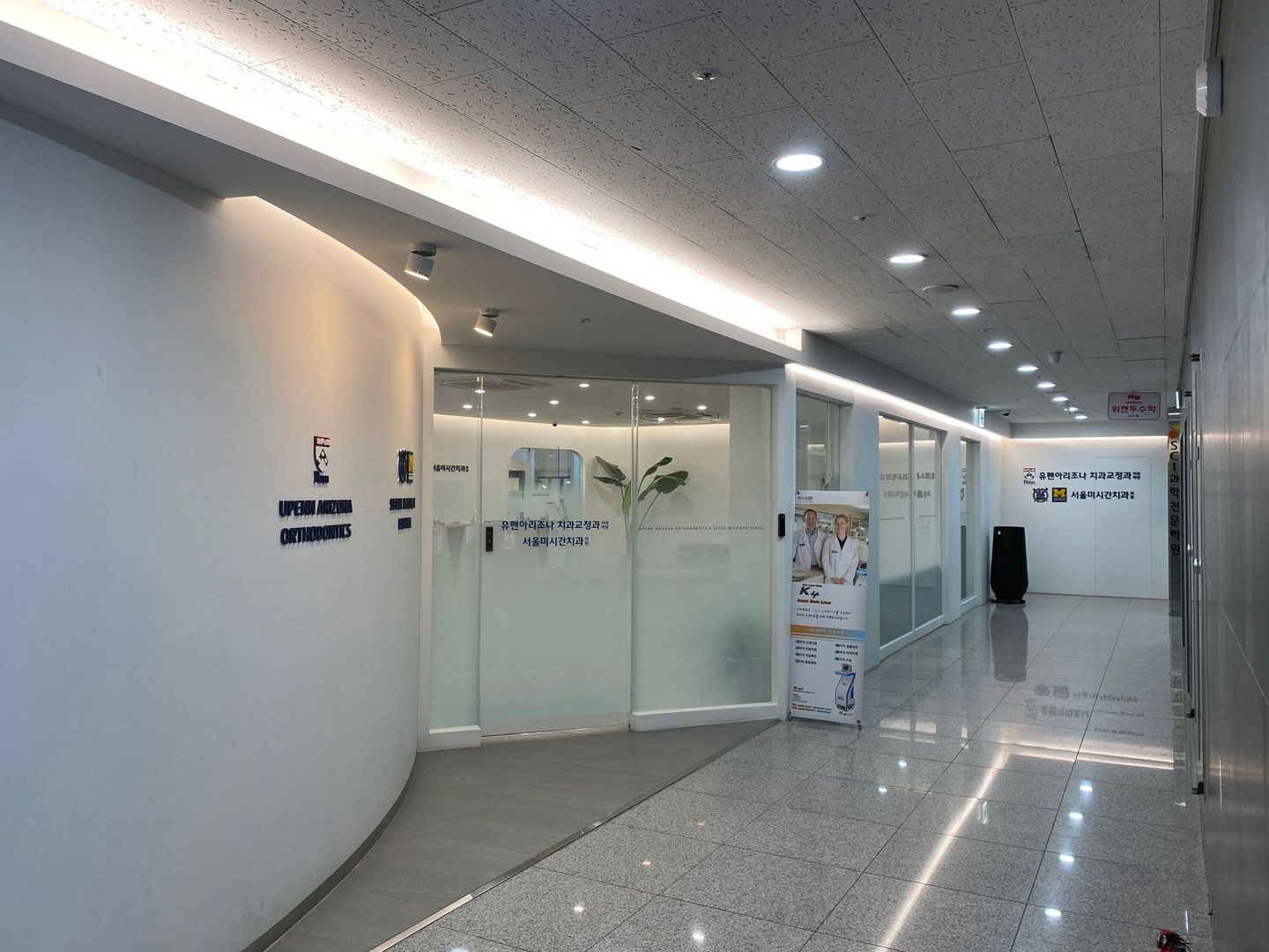 A long hallway with a white wall and a glass door