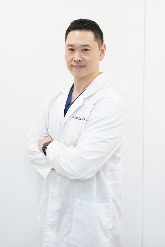 A man in a white lab coat is standing with his arms crossed.