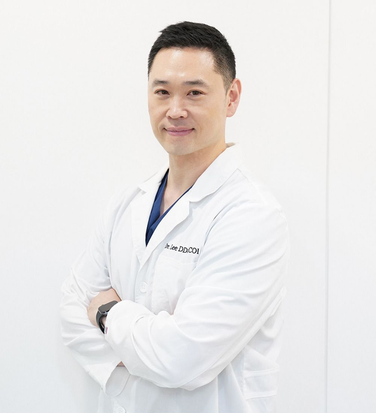 A man in a white lab coat is standing with his arms crossed.