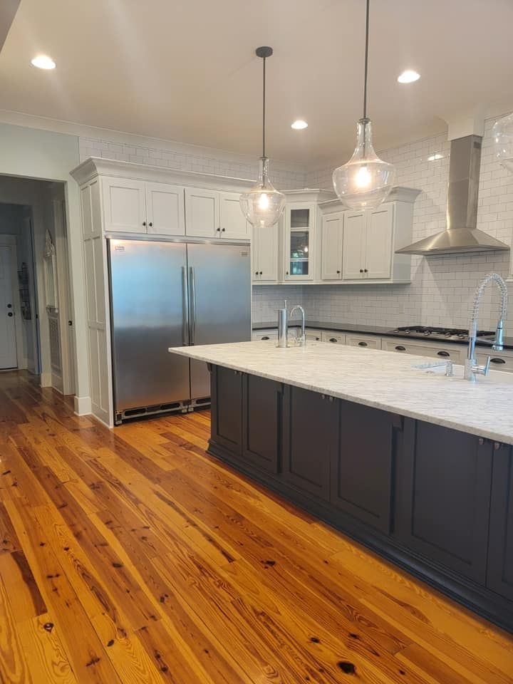 Kitchen with wood floor, stainless steel fridge, dark island with marble countertop, and pendant lights.