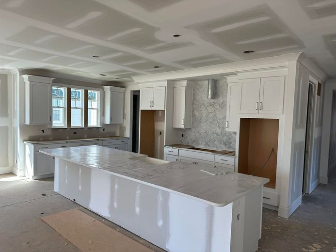 Kitchen under construction, white cabinets, island, and drywall ceilings and walls.