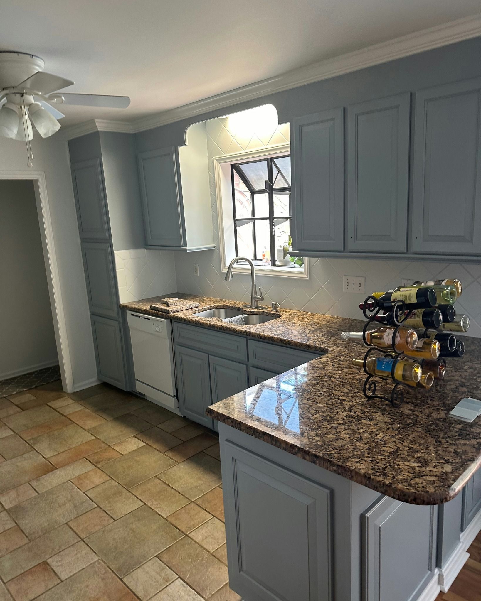 Blue cabinets and granite countertops in a kitchen with a window and wine rack.