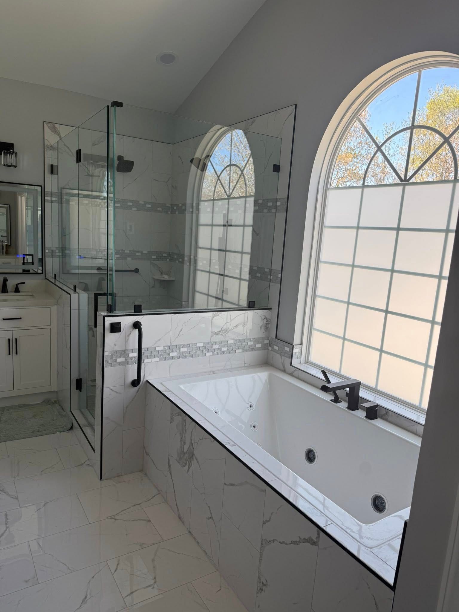 Bathroom with white marble tile, glass shower, soaking tub under arched windows.