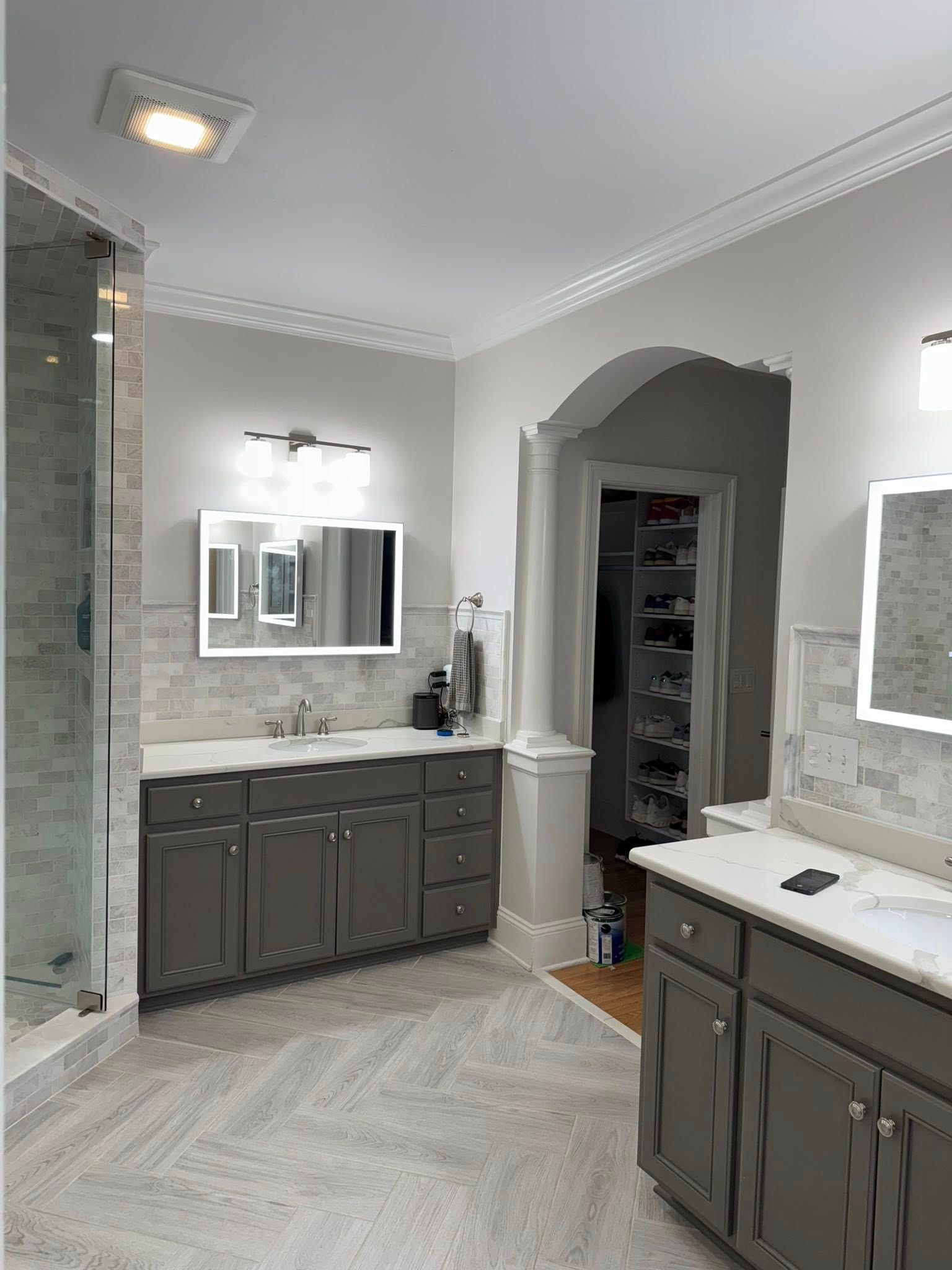 Bathroom with gray cabinets, white countertops, large mirrors, and a walk-in closet.