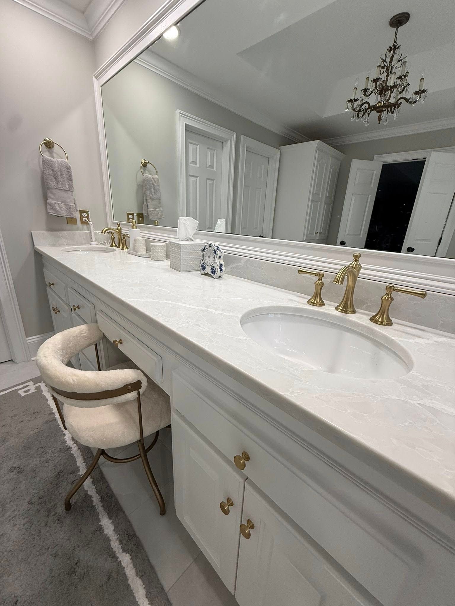 Elegant white bathroom with vanity, gold fixtures, and a chandelier.