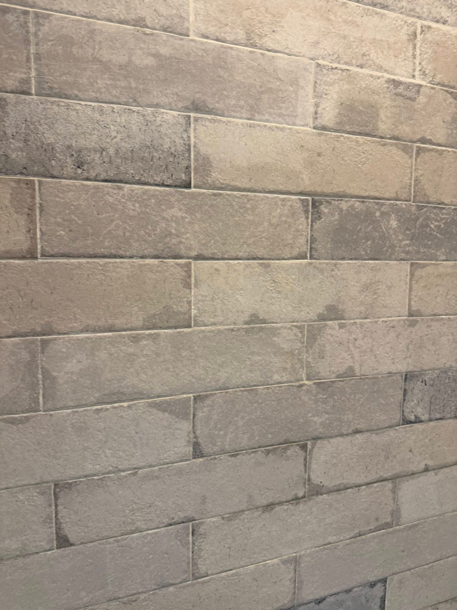 Gray brick wall with a textured surface, tiles arranged in a staggered pattern.