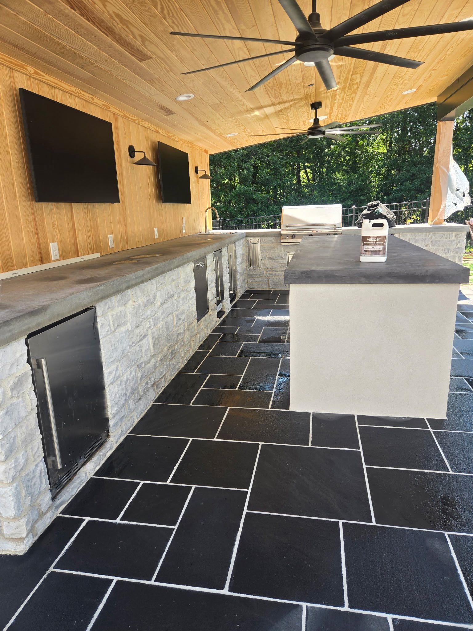 Outdoor kitchen with dark floor tiles, stone counter, and ceiling fans.