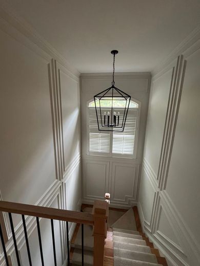 Stairwell with white walls and trim, shutters, and a chandelier. A wooden railing is visible.