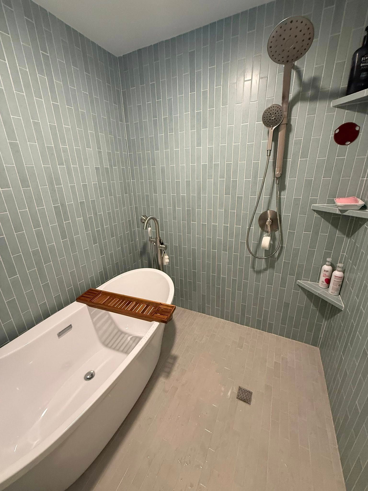Modern bathroom with a white tub, shower with multiple heads, and glass shelves. Blue tiled walls.