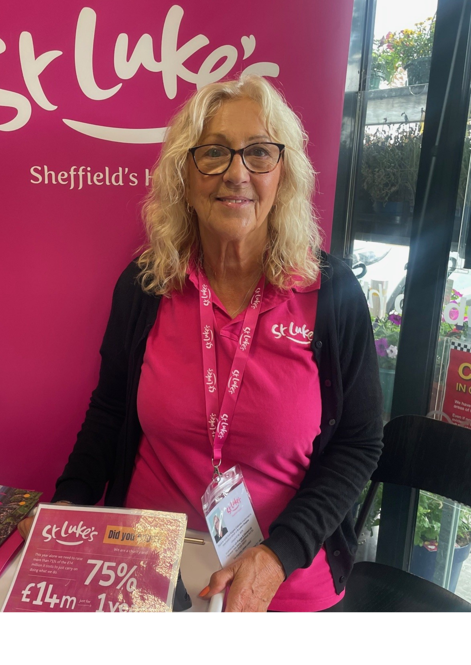 Woman in pink polo shirt and black leggings, in front of a St. Luke's Hospice banner.