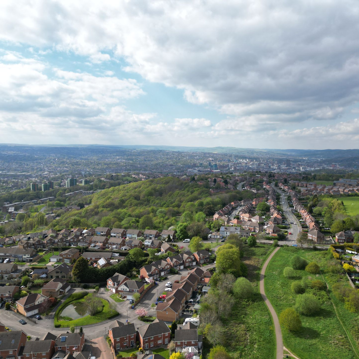 Aerial view of a town with houses, green trees, and a cloudy sky.