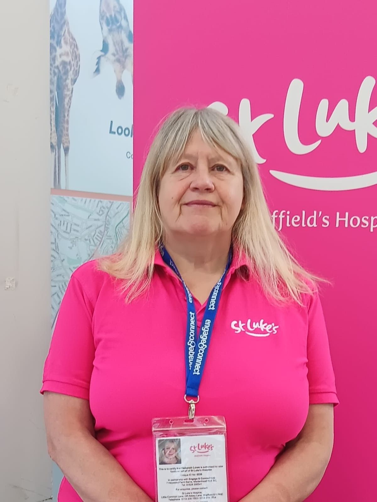 Woman in pink polo shirt, badge, in front of pink St Luke's Hospice backdrop.