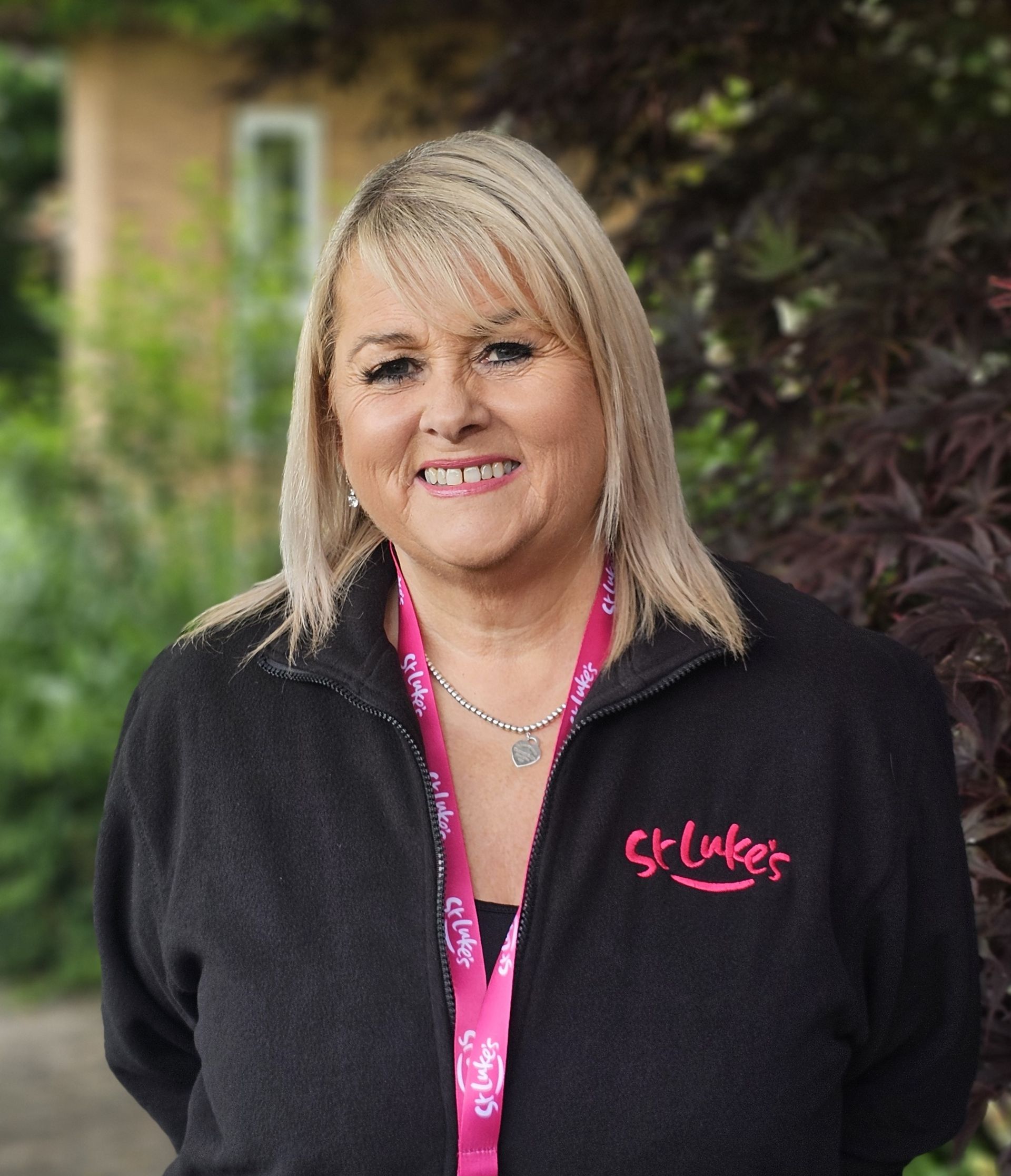 Woman wearing a black St Luke's jacket, smiling outdoors with a pink lanyard.
