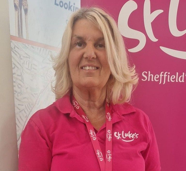 Woman in pink St. Luke's shirt, smiles at the camera. She stands in front of a pink St. Luke's banner.