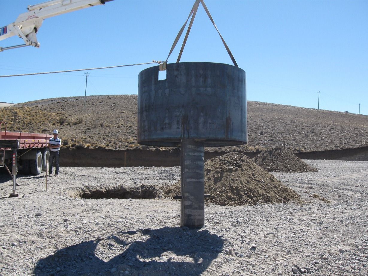 Grúa levantando una gran estructura cilíndrica de hormigón sobre un sitio de construcción.