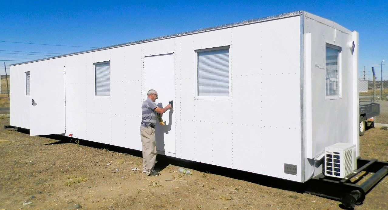 Hombre de pie junto a un edificio portátil blanco con ventana, puerta y aire acondicionado.