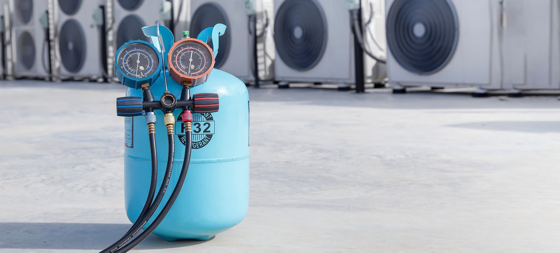A cylinder of refrigerant is sitting on the ground in front of a row of air conditioners.