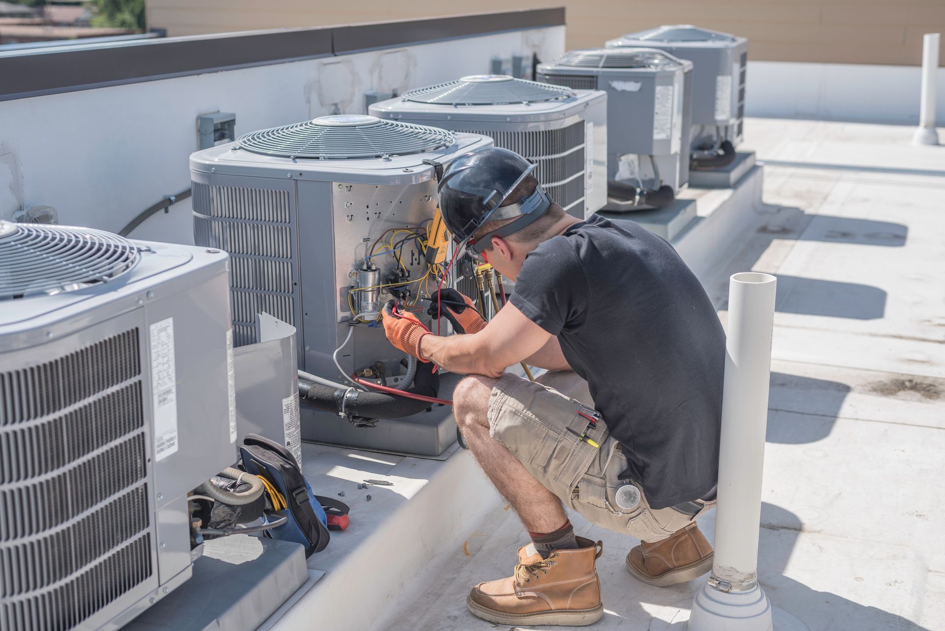 A man is working on an air conditioner on the roof of a building.