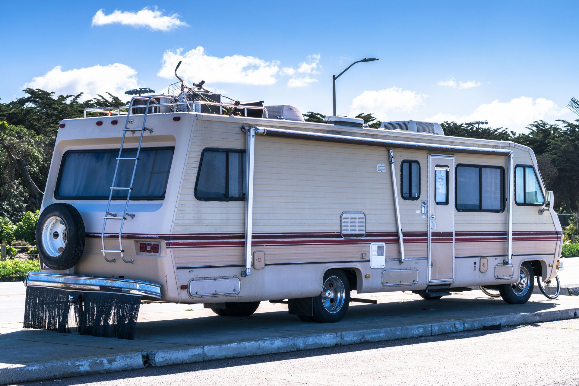 Beige and pink RV parked outdoors on a sunny day, with a bicycle rack on top.