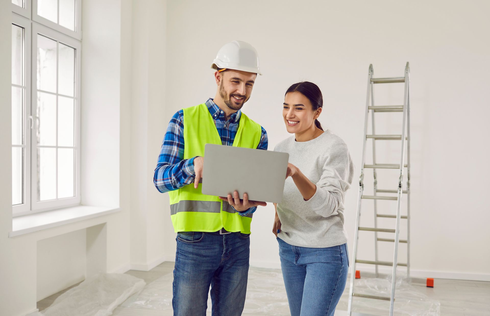 Builder and homeowner reviewing plans in a bright, unfinished room with a ladder nearby