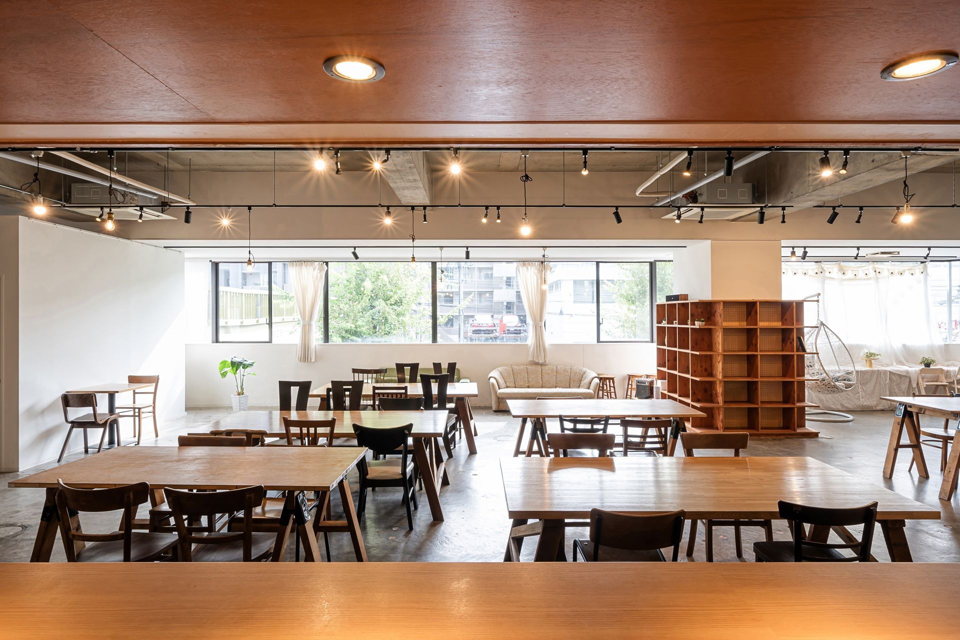 Bright modern café with wooden tables, chairs, pendant lights, and large windows.