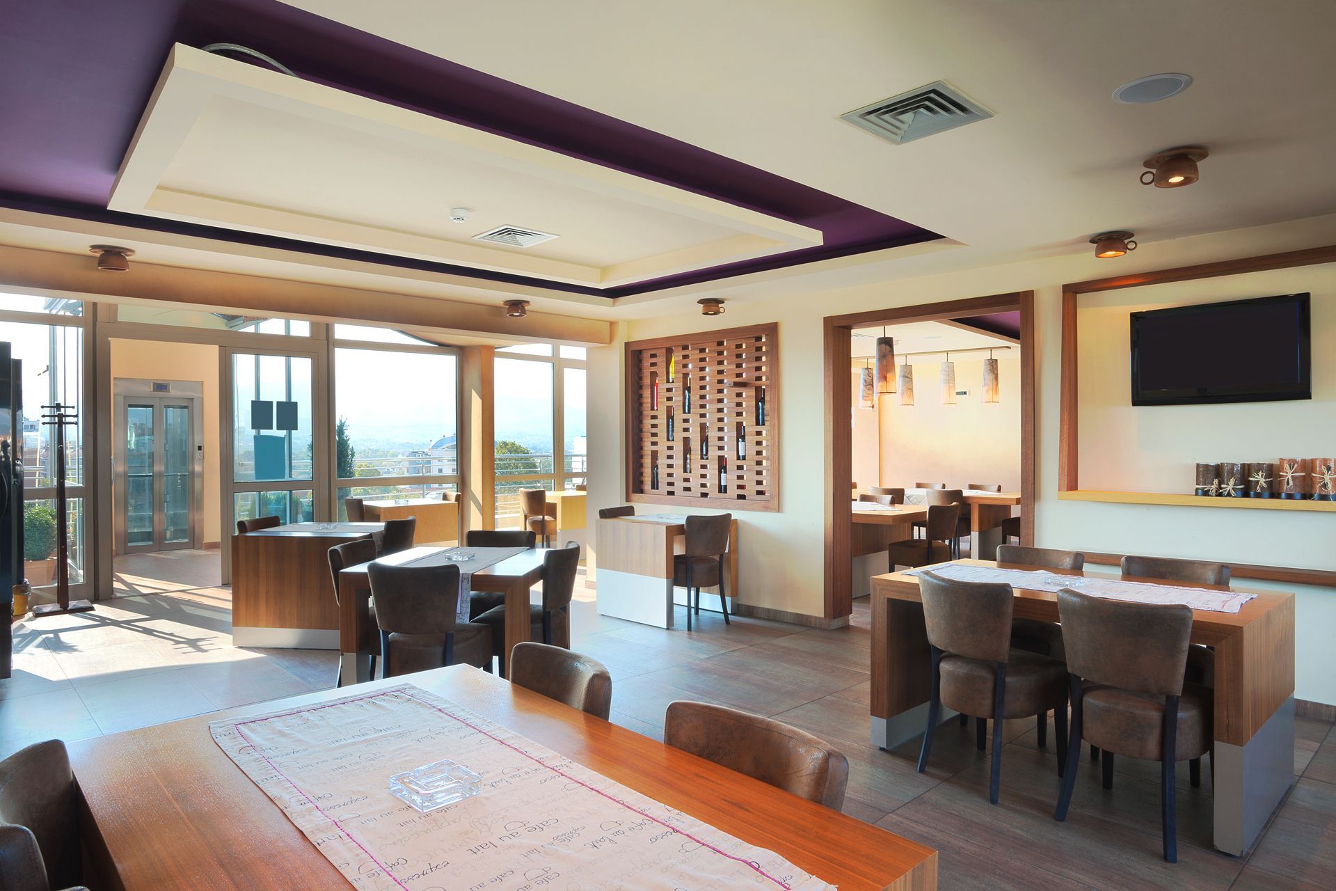 Bright modern restaurant dining room with wooden tables, chairs, and large windows overlooking water