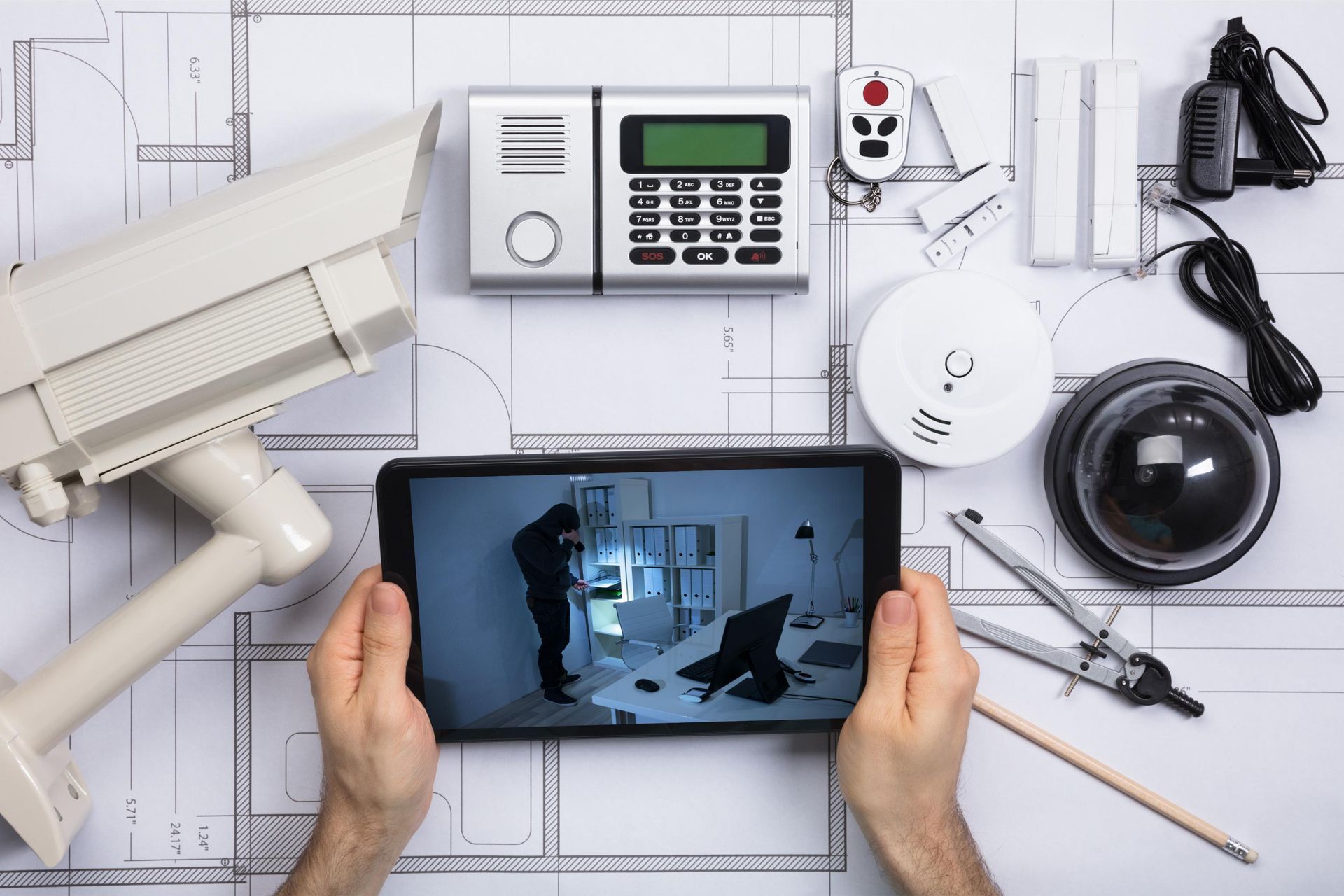 Security camera equipment on tiled wall, with tablet showing live home surveillance feed