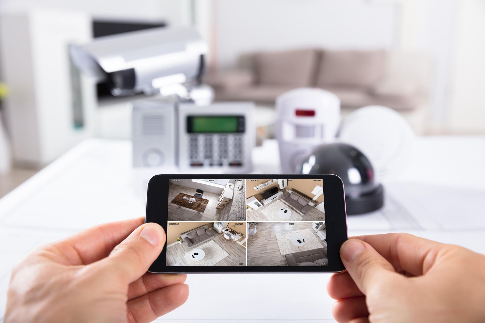 Hands holding a smartphone showing security camera feeds in a bright home interior